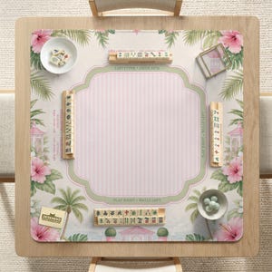 May include: A square mahjong mat featuring a light pink striped center, surrounded by a border of pink hibiscus flowers, green palm leaves, and small gazebos. The mat includes wooden tile racks, a white bowl with tiles, and a small bowl with green dice.