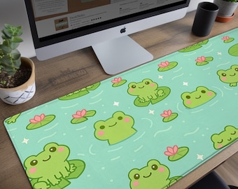 Puede incluir: Alfombrilla de escritorio estética con un patrón repetido de ranas de dibujos animados sobre nenúfares en un estanque. La alfombrilla es de color verde claro con flores de loto rosas y estrellas blancas. El texto "Aesthetic Desk Mats and Mouse Pads" es visible en la pantalla del ordenador.