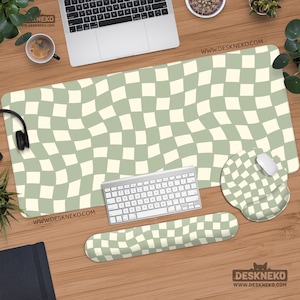 May include: A desk setup featuring a large, sage green and cream checkered pattern desk mat, a matching mousepad with wrist rest, and a wrist rest. A keyboard, mouse, and headphones are also present.