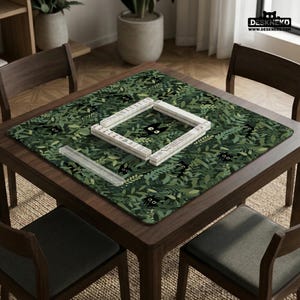 May include: A square mahjong table mat with a green leaf pattern and black cat silhouettes. White mahjong tiles are arranged in a square, with a clear plastic tile holder. The table is made of dark wood, with matching chairs. The logo "DESKNEKO" is in the top right corner.