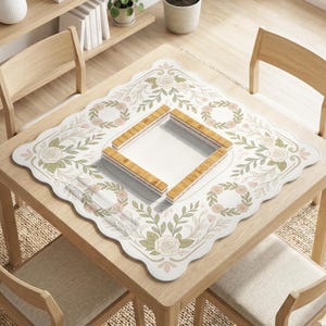 May include: A square mahjong mat with a scalloped edge featuring a white background decorated with light green and soft pink floral rose patterns and circular wreaths. In the center sits a square wooden mahjong tile rack set.