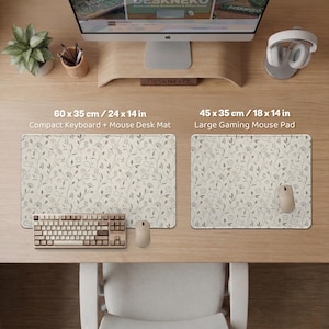 Pu&ograve; includere: Due tappetini da scrivania rettangolari con sfondo color crema e un delicato motivo floreale e di viticci grigio scuro. Il tappetino sinistro misura 60 x 35 cm, quello destro 45 x 35 cm. Entrambi sono posizionati su una scrivania in legno.
