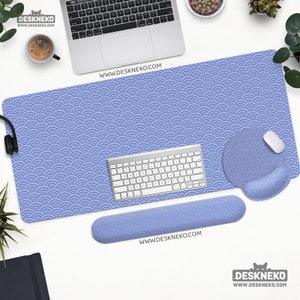 May include: A desk setup with a blue wave-patterned desk mat, mousepad, and wrist rest. A white keyboard and mouse are on the mat. The website address www.DESKNEKO.COM is printed on the mat and wrist rest.