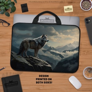 May include: Laptop sleeve featuring a majestic wolf standing on a rocky cliff, overlooking a mountain range. The design is printed on both sides. The sleeve has a black handle and is on a wooden surface.