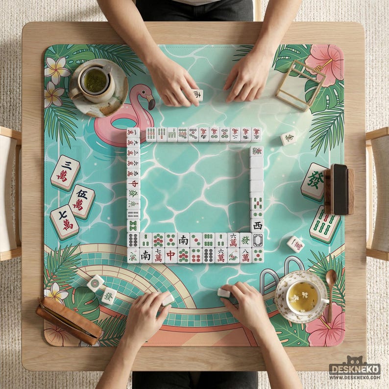 May include: A top-down view of a Mahjong game in progress. The game is set on a wooden table with a tropical-themed mat featuring a pool design, a pink flamingo float, and floral accents. The tiles are arranged in a square, with players' hands visible.