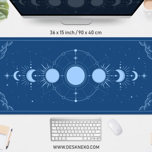 May include: A rectangular desk mat with a celestial design. The mat is dark blue with a light blue illustration of the sun, moon phases, and stars. The mat measures 36 x 15 inches (90 x 40 cm). The website address www.deskneko.com is printed at the bottom.