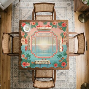 May include: A square mahjong mat featuring a tropical sunset design with pink flamingos, green palm leaves, and red hibiscus flowers. The center displays game instructions and charts, surrounded by four wooden tile racks and a small white bowl.