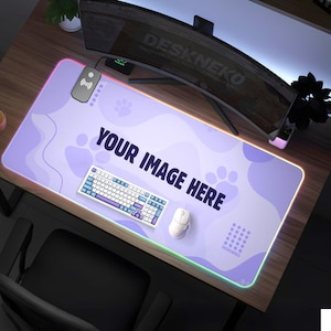 May include: A rectangular, light purple desk mat with a glowing, multi-colored edge. The mat features the text "YOUR IMAGE HERE" and paw prints. A white keyboard and mouse are on the mat. The brand name "DESKNEKO" is also visible.