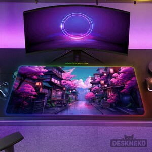 May include: A rectangular gaming mouse mat featuring a Japanese landscape with pink cherry blossom trees and traditional buildings. The mat has a colourful LED edge and the text "DESKNEKO.COM". A curved monitor is above the mat.