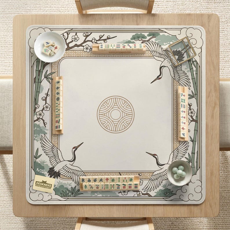 May include: A square mahjong table with a cream-colored playing surface featuring a crane design and bamboo accents. The table includes tiles, bowls, and a decorative border. The table is set on a light wood frame.