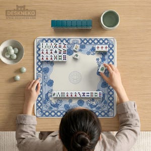 May include: A person playing Mahjong on a blue and white patterned mat. The game set includes tiles, a rack, and a small bowl. The mat features a floral and koi fish design. The game is set on a wooden table.
