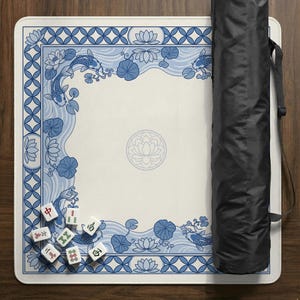 May include: A white Mahjong mat with a blue and white koi fish and lotus flower design. The mat has a decorative border and a central lotus flower emblem. A black carrying case is on the right side of the mat. Mahjong tiles are visible.