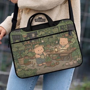 May include: A black laptop bag with a whimsical illustration of two bear characters in a greenhouse tending to plants. The bag has a top handle, a shoulder strap, and the text "DESKNEKO". The background is a lush green with potted plants.