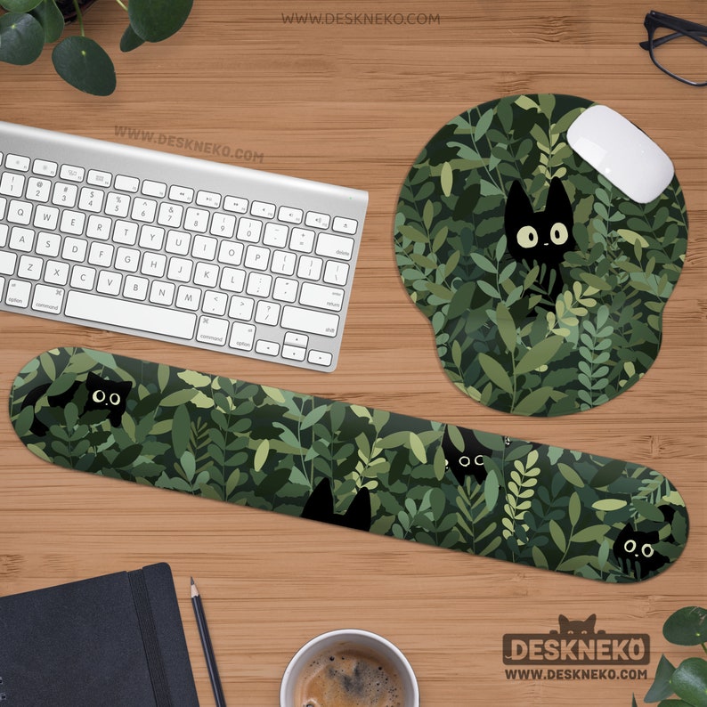 K&ouml;nnte beinhalten: Ein Computer-Schreibtisch-Setup mit Tastatur, Maus und Handgelenkauflage. Das Zubeh&ouml;r hat ein gr&uuml;nes Bl&auml;ttermuster mit schwarzen Katzen-Silhouetten. Ein rundes Mauspad mit dem gleichen Design ist ebenfalls vorhanden. Die Website-Adresse "WWW.DESKNEKO.COM" ist sichtbar.
