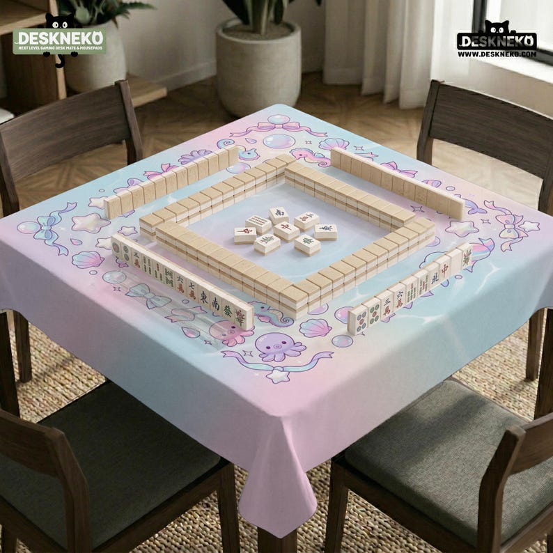May include: A pastel-colored tablecloth with a whimsical design featuring sea creatures and bows. Wooden Mahjong tiles are arranged on the table. The text "DESKNEKO" is visible in the top left and right corners.
