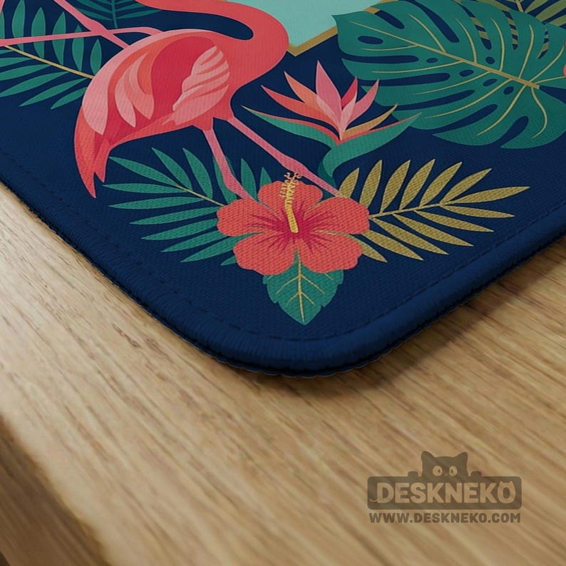 May include: A navy blue desk mat featuring a flamingo, tropical flowers, and foliage. The design includes a red flamingo, a red hibiscus flower, and green leaves. The mat has a dark blue border and the text "DESKNEKO" and "WWW.DESKNEKO.COM" in the bottom right corner.