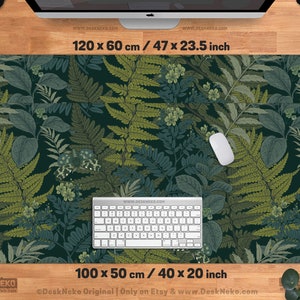 Pu&ograve; includere: Un grande tappetino da scrivania rettangolare con un design botanico con felci e altro fogliame in tonalit&agrave; di verde e blu. Il tappetino misura 120 x 60 cm e 100 x 50 cm. Una tastiera e un mouse bianchi sono sul tappetino.