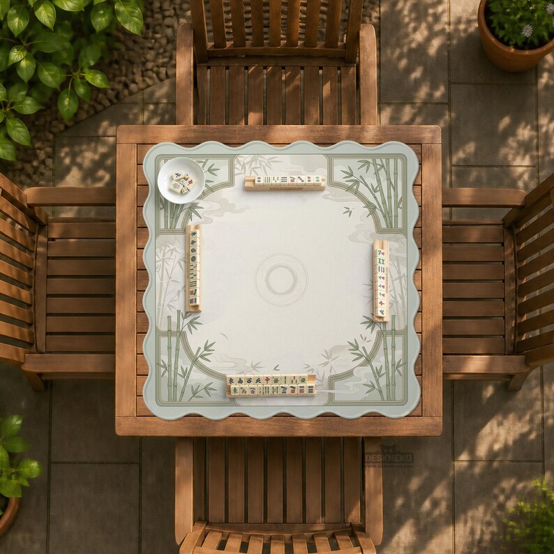 May include: A square mahjong mat with scalloped edges featuring a light gray center and a green bamboo border design. The mat includes four wooden tile racks placed around the perimeter, each holding a set of mahjong tiles, and a small white bowl.