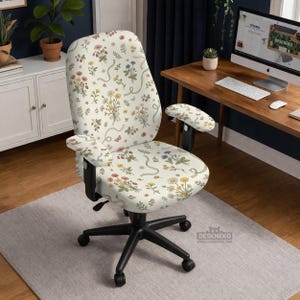 Könnte beinhalten: Ein Bürostuhl mit cremefarbenem Blumenmuster, das verschiedene Blumen, Schmetterlinge und Bänder zeigt. Der Stuhl hat ein schwarzes Gestell und Armlehnen und steht vor einem neutralen Teppich und einem Holzschreibtisch.