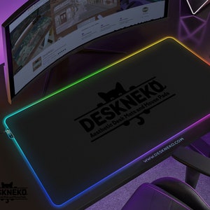 Op de afbeelding: Zwart rechthoekig DESKNEKO-muismat met een kleurrijke LED-rand. De mat heeft het DESKNEKO-logo en de tekst "Aesthetic Desk Mats and Mouse Pads". De website www.DESKNEKO.COM is ook zichtbaar.
