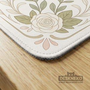 May include: A rectangular mouse pad with rounded corners featuring a white background and a central line-art illustration of a rose surrounded by sage green leaves and delicate tan flourishes. The edges are finished with white stitched borders.