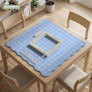 May include: A light blue, scalloped-edge mat with a white geometric pattern covers a wooden table. Mahjong tiles are arranged in a square, with additional tiles and a clear acrylic piece nearby. The text "DESKNEKO" is visible in the top left corner.