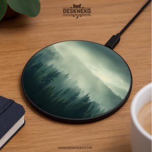 Puede incluir: Un cargador inalámbrico redondo con un diseño de bosque. La imagen muestra un bosque brumoso con árboles verdes y un cielo claro. El cargador tiene un borde y un cable negros. El logotipo y el sitio web de DeskNeko son visibles.