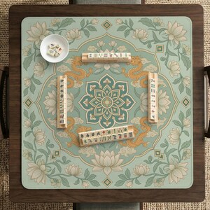 May include: A square mahjong mat featuring a light green background with a central lotus mandala, golden dragon illustrations, and floral motifs. Four wooden tile racks are arranged in a square, with a small white bowl containing mahjong tiles.