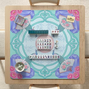 May include: A square mahjong game mat with a teal and light blue design featuring peacock illustrations, fans, and floral accents. The mat is set up with tiles, ready for play. A small bowl of white balls is in the corner.