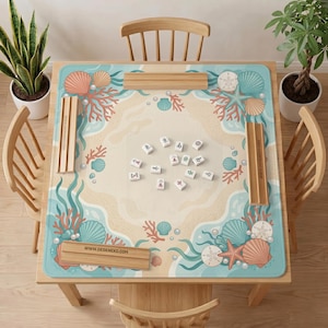 May include: A square mahjong mat featuring a beach-themed illustration with coral, seashells, starfish, and sand dollars in shades of blue, peach, and cream. Four wooden tile racks are placed on the mat, which displays the text www.deskneko.com.