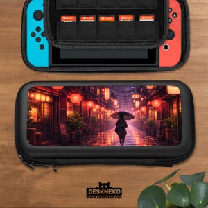 Puede incluir: Funda de transporte negra con cremallera para consola de juegos, con una vibrante ilustración de una persona con paraguas caminando por una calle lluviosa con faroles. La funda está abierta, mostrando la consola y los cartuchos de juego.