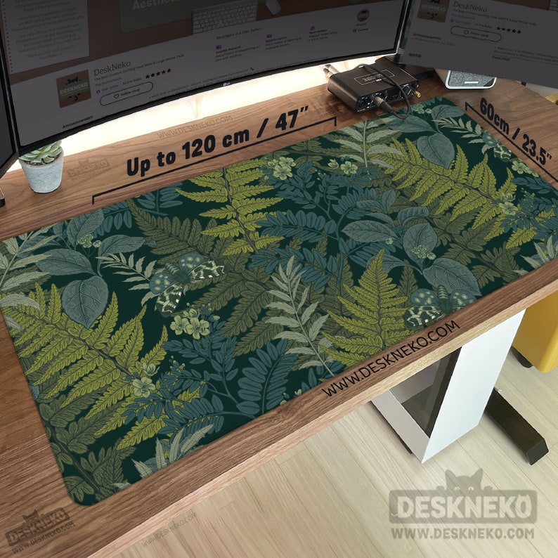 Pu&ograve; includere: Un tappetino da scrivania rettangolare con un motivo botanico di felci nelle tonalit&agrave; del verde e del blu. Il tappetino misura fino a 120 cm di lunghezza e 60 cm di larghezza. Il nome del marchio "DeskNeko" e l'indirizzo del sito web sono stampati.