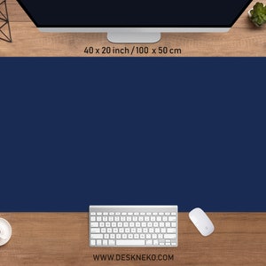 May include: A navy blue desk mat, measuring 100 x 50 cm, with rounded corners, is displayed on a wooden desk. A white keyboard, mouse, and coffee cup are visible. The website address www.deskneko.com is printed at the bottom.