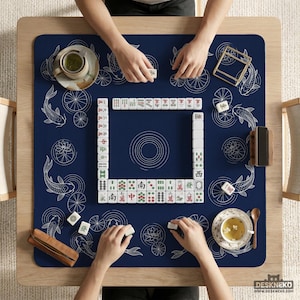 Puede incluir: Vista superior de un juego de Mahjong en curso sobre una mesa de madera. La alfombra azul marino presenta dise&ntilde;os de peces koi y flores de loto blancos. Se ven las manos de los jugadores, sosteniendo fichas. Tazas de t&eacute; y un soporte de fichas de madera.