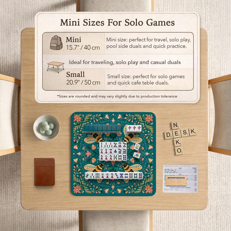 May include: A square teal mahjong mat with a floral and bee pattern, featuring white mahjong tiles with red and black characters. Includes a sign labeled Mini Sizes For Solo Games, a small bowl of white spheres, a brown notebook, and wooden letter tiles.