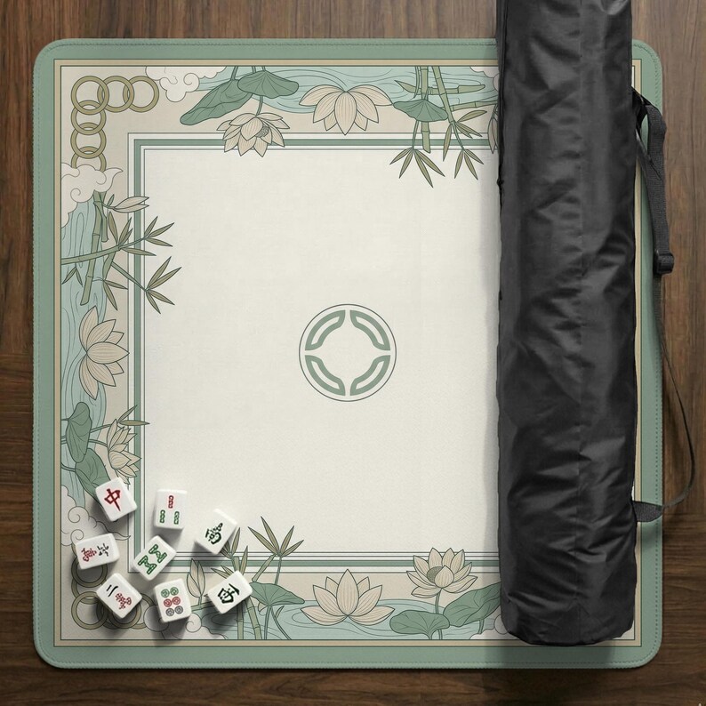 May include: A rectangular Mahjong game mat with a cream-colored center and a light green border. The border features a floral and bamboo design. A black carrying case is on the right side. Several white Mahjong tiles are visible on the mat.