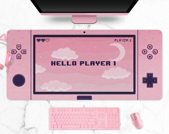 May include: Pink gaming desk mat with a retro video game console design. The mat features a screen with the text "HELLO PLAYER 1", clouds, and a moon. Includes a keyboard, mouse, and headphones.