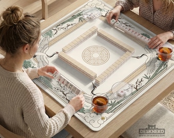 May include: A square mahjong game table with a cream-colored playing surface featuring a crane and floral design. The table is made of wood and has a decorative border. Two people are playing mahjong, with tiles and tea cups visible.