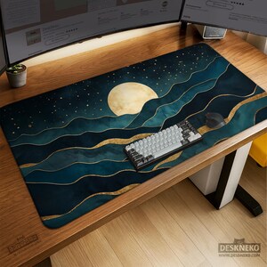 May include: A large rectangular desk mat with a night sky design, featuring a full moon, stars, and teal and gold wave patterns. A white keyboard and black mouse are on the mat. The mat has the text "DESKNEKO" on the bottom right.