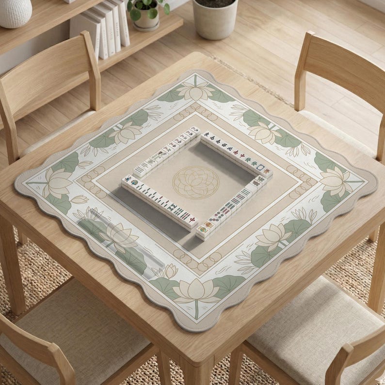 May include: A square wooden table with a beige and green floral patterned mat. The mat features lotus flowers and a central square with a lotus design. Mahjong tiles are arranged on the mat, suggesting a game in progress.