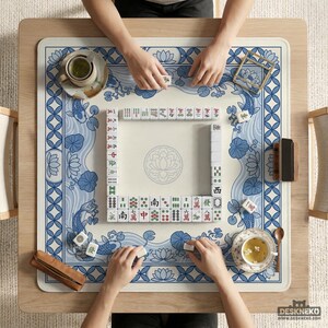 May include: Overhead view of a Mahjong game in progress. The game is set on a light wood table with a blue and white patterned mat. The mat features koi fish and lotus flower designs. Players are arranging tiles, with tea cups and accessories nearby.