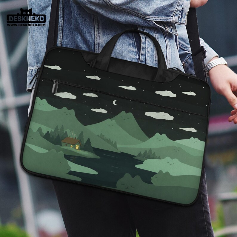 May include: A black laptop bag with a landscape design featuring a house, mountains, river, clouds, and stars. The bag has a handle and a shoulder strap. The brand name "DESKNEKO" is visible in the top left corner.