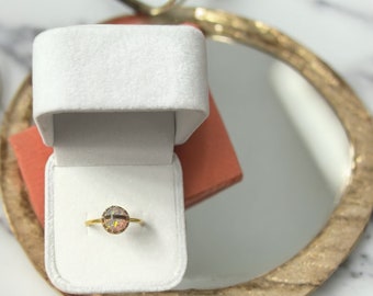May include: A gold ring with a round, iridescent opal gemstone set in a white velvet ring box.