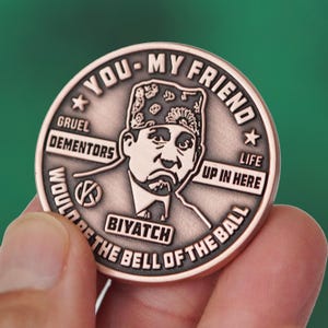 Puede incluir: Una moneda de color cobre con el texto "YOU - MY FRIEND" y "WOULD BE THE BELL OF THE BALL". La moneda presenta un retrato de un hombre con un tocado estampado. También es visible el texto "GRUEL DEMENTORS" y "BIYATCH".