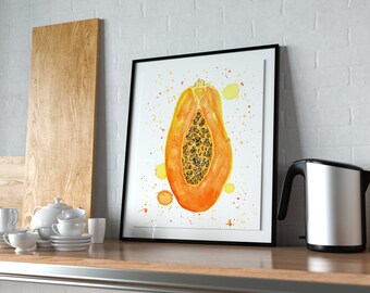 Puede incluir: Una impresión en acuarela enmarcada de media papaya, que muestra tonos vibrantes de naranja y amarillo con semillas negras. La obra de arte se exhibe en una estantería de madera junto a una tetera eléctrica plateada, tazas de té blancas y una tabla de cortar de madera.
