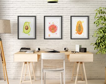 Puede incluir: Tres pinturas de acuarela enmarcadas de fruta cortada en una pared de ladrillo blanco. Las pinturas son de un aguacate, un higo y una papaya. Las pinturas están colgadas sobre un escritorio de madera con una computadora portátil, libros y dos altavoces.