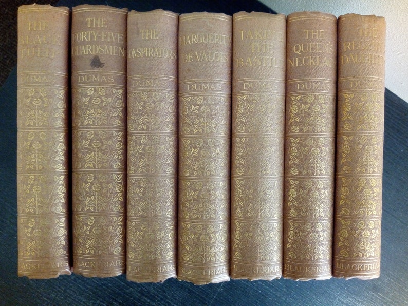Puede incluir: Una colecci&oacute;n de siete libros antiguos con cubiertas de color marr&oacute;n claro y letras doradas. Los t&iacute;tulos incluyen "El tulip&aacute;n negro" y "El collar de la reina". Las lomos presentan patrones florales y el nombre del autor, Dumas.