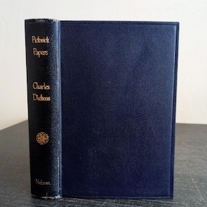Pode incluir: Um livro de capa dura azul-escuro intitulado Pickwick Papers de Charles Dickens, publicado pela Nelson. A lombada apresenta letras douradas e um pequeno emblema circular dourado. A capa tem um acabamento texturizado com um design de borda.