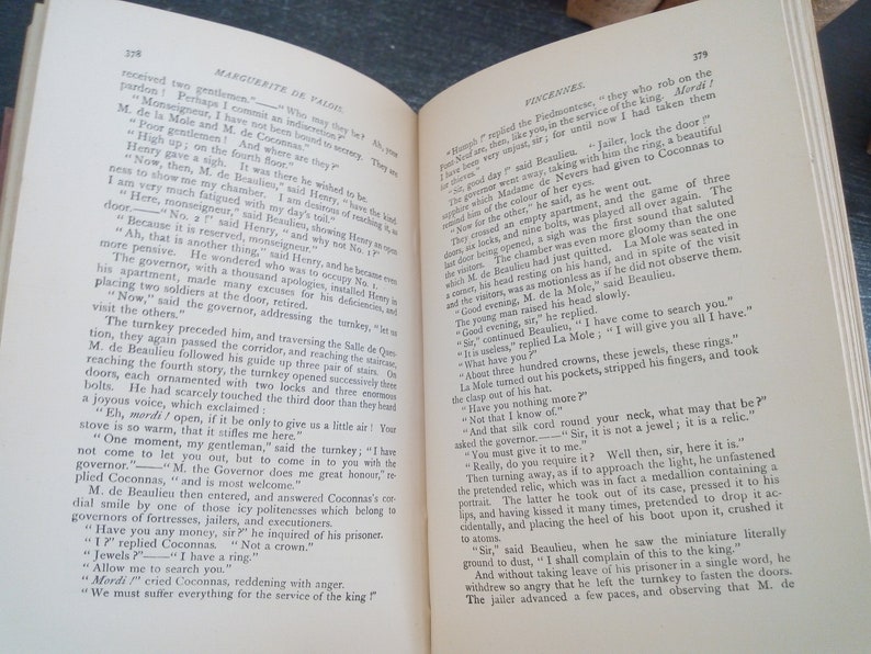 Puede incluir: Un libro abierto con p&aacute;ginas amarillentas y texto impreso. Las p&aacute;ginas est&aacute;n envejecidas, lo que sugiere la edad. El libro parece ser un texto hist&oacute;rico o una novela, con t&iacute;tulos de cap&iacute;tulos visibles.
