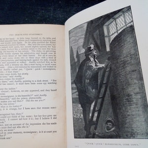 Puede incluir: Un libro abierto con una ilustraci&oacute;n en blanco y negro de un hombre subiendo una escalera. La ilustraci&oacute;n est&aacute; junto al texto. El texto dice: "Quick! Quick! Monseigneur, Come Down."